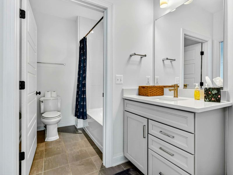 Guest Bathroom - Nautical anchor shower curtain, white vanity with gold faucet, and a tub-shower combo with a lake-house feel.