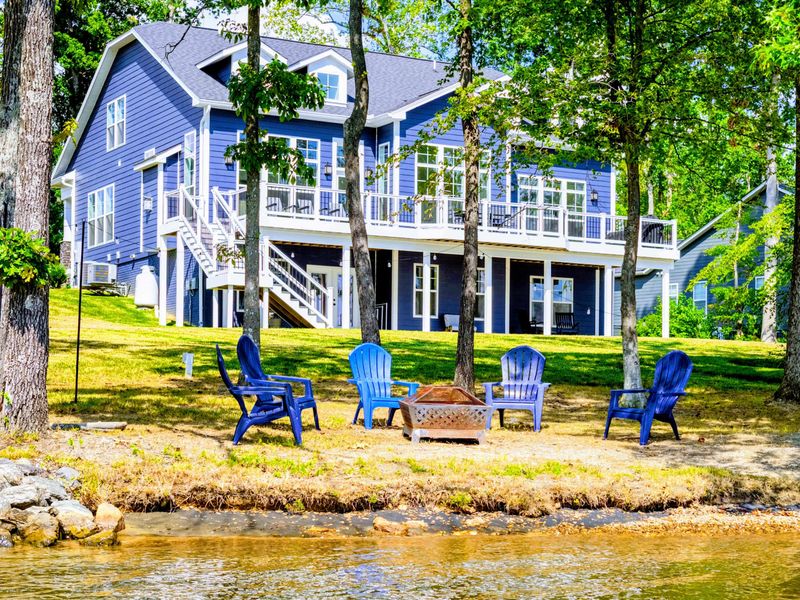 Lakefront Exterior - The blue Craftsman home rises above its private waterfront, with the fire pit and sandy beach steps from the lake.