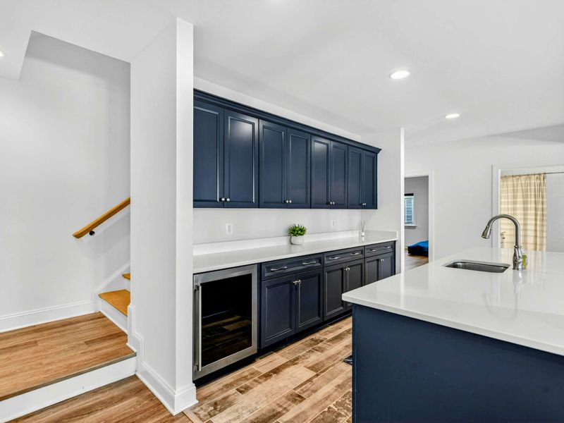 Wet Bar Kitchenette - Full bar with navy cabinets, wine cooler, dishwasher, and bar seating tucked at the base of the stairs.