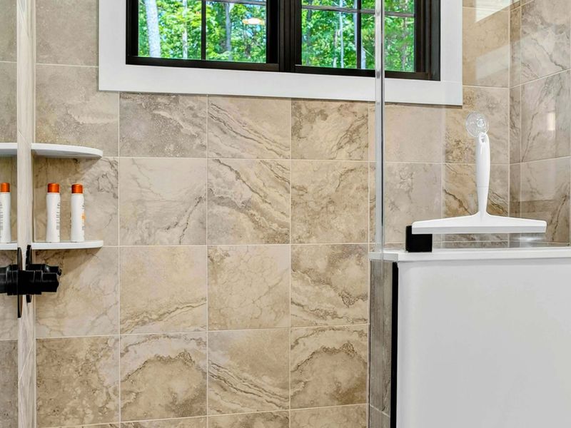 Primary Bathroom - Shower detail showing the rain head, natural stone tile, and glass enclosure.