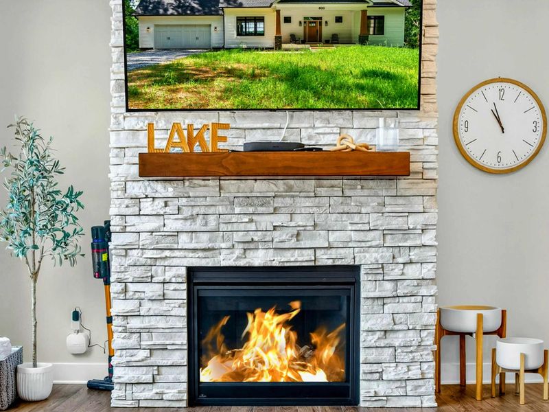 Great Room - Stone gas fireplace with wood mantel, mounted Smart TV, and LAKE letters on the hearth.