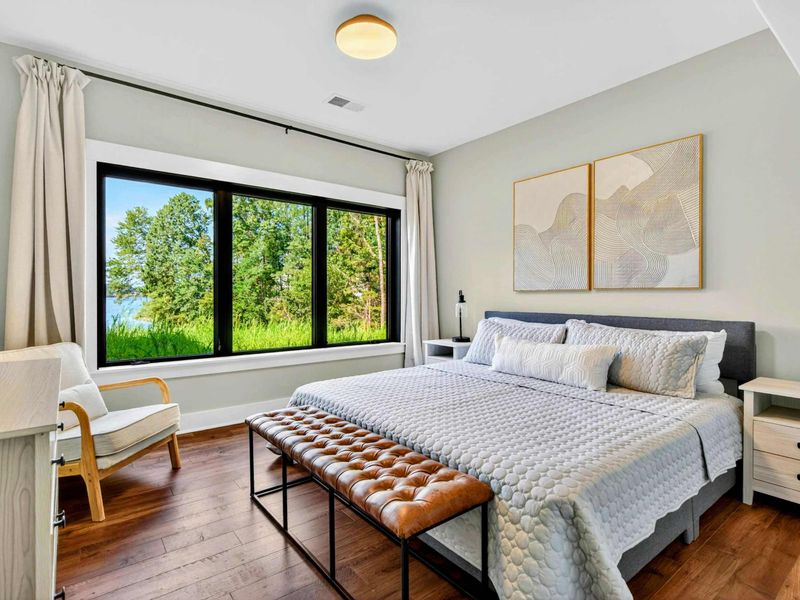Bedroom 5 - Lake level king suite with dark headboard, leather bench, and lake views through large windows.