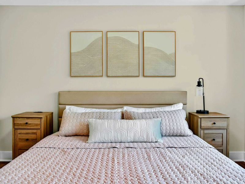 Bedroom 3 - King bed with blush pink bedding and wave-inspired triptych art above oak nightstands.