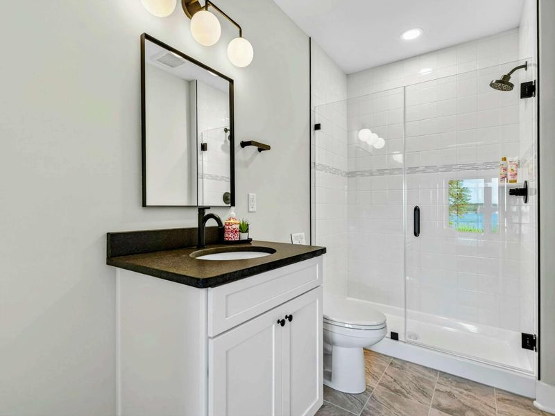 Bathroom 5 - Single vanity with globe sconces and a glass-enclosed walk-in shower.