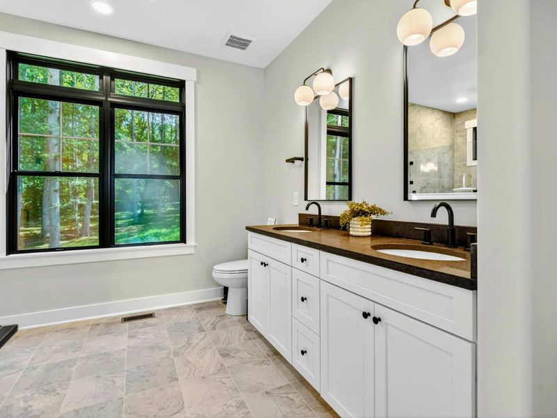 Primary Bathroom - Double vanity with white cabinetry, dark stone counter, and globe sconce lighting.