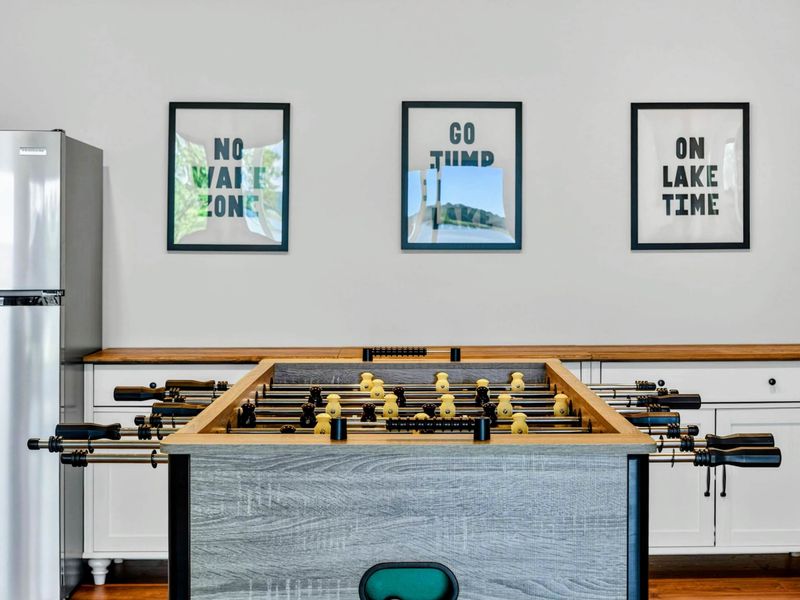 Game Room - Foosball table with lake-themed wall art, mini fridge, and white built-in cabinets.