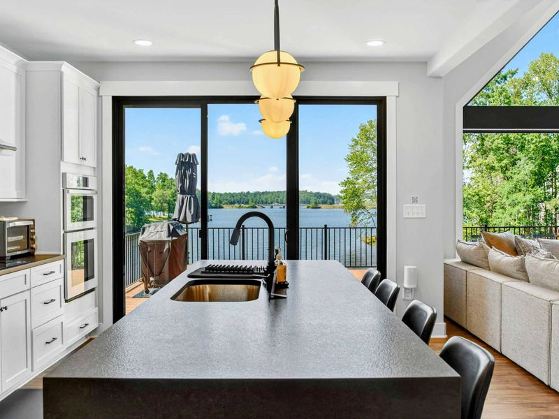 Kitchen - Large island with black bar stools and globe pendant lights, sliding door opens to the deck and lake.
