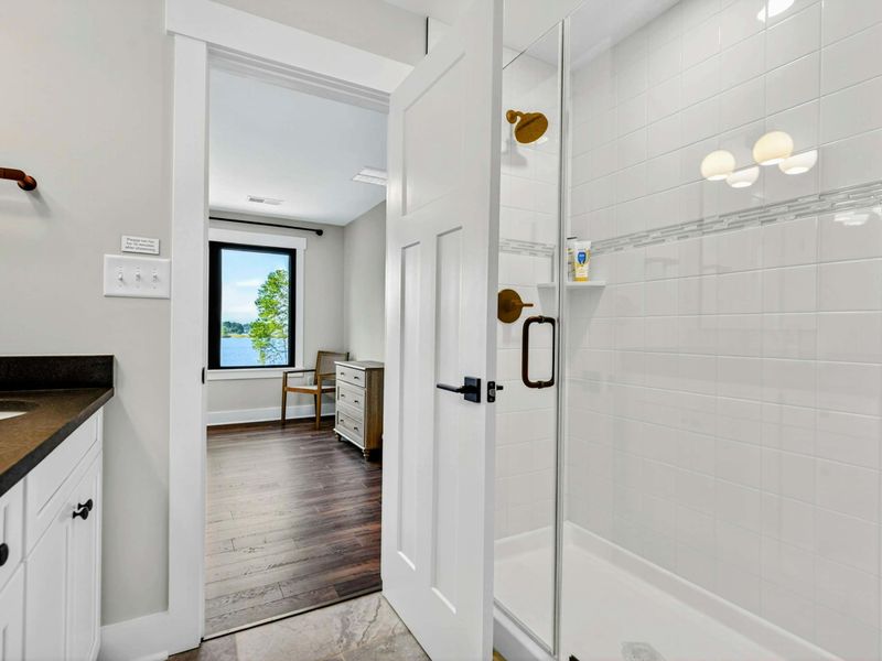 Bathroom 3 - Walk-in shower with white subway tile and accent band, glass door, view through to bedroom.