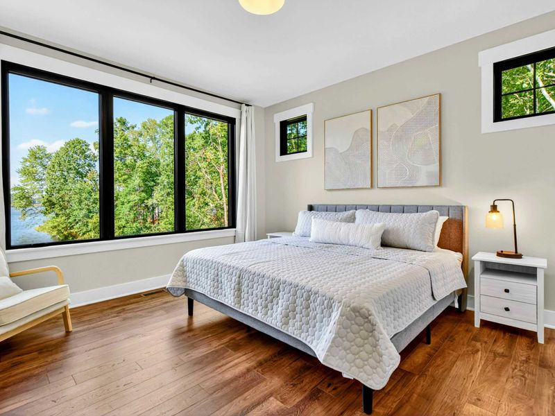 Primary Suite - King bed with upholstered headboard, abstract art, and an accent chair beside lake view windows.