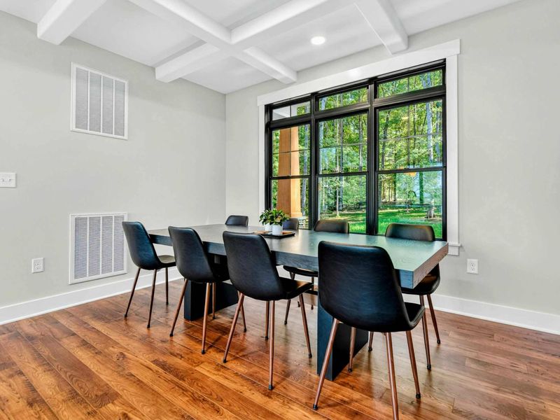 Dining Area - Dark wood table with seating for eight beneath a coffered ceiling and large window.
