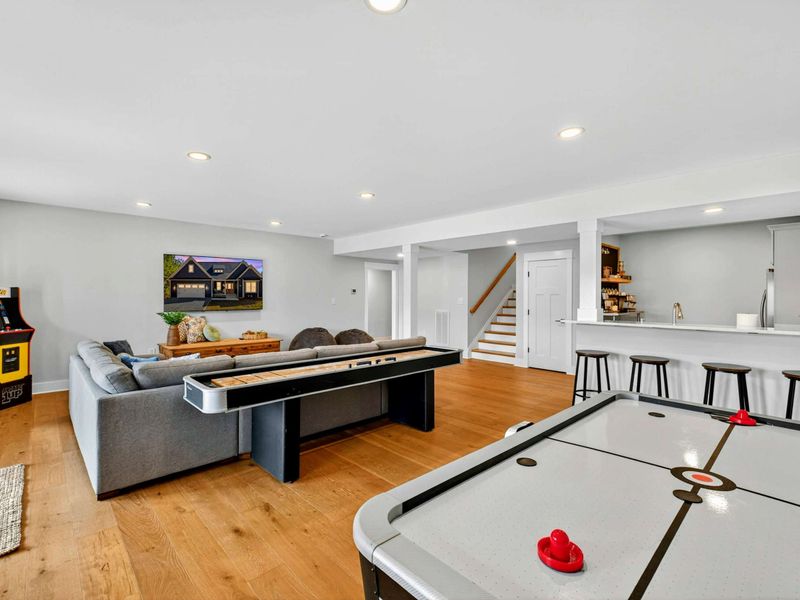 Game Room Wide - Air hockey, shuffleboard, the arcade cabinet, sectional, Smart TV, and the second kitchen bar with stools, all in one open lower-level space.