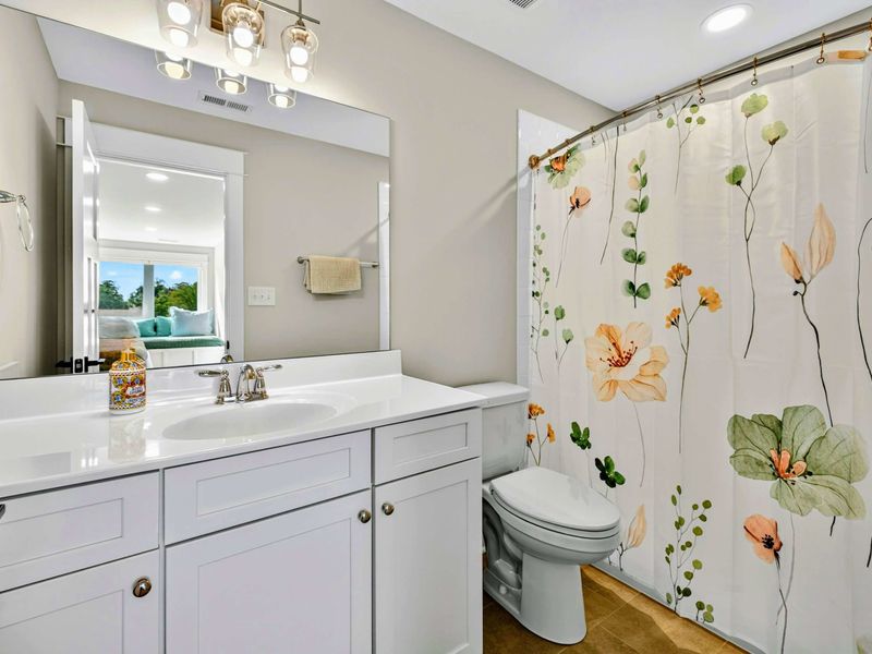 Upper Ensuite - A white vanity with quartz countertop, floral shower curtain, and the Inglenook window seat reflected in the mirror.