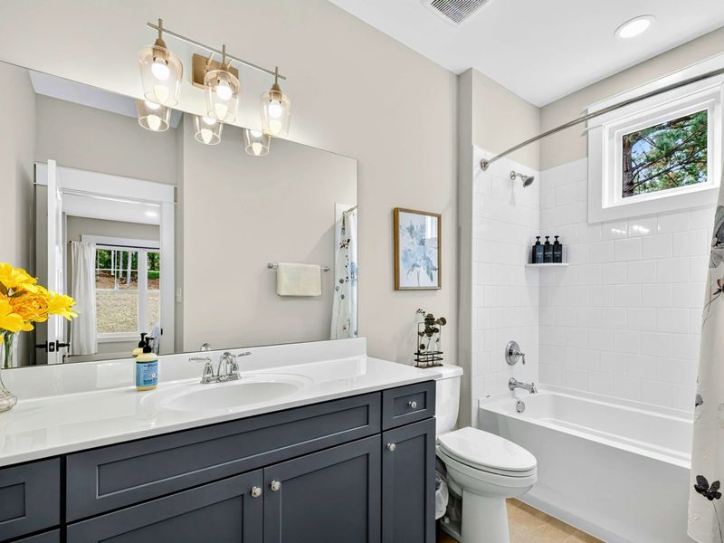 Main Level Ensuite - A navy vanity with quartz counterto, a floral shower curtain, and fresh flowers in this lower-level bathroom.