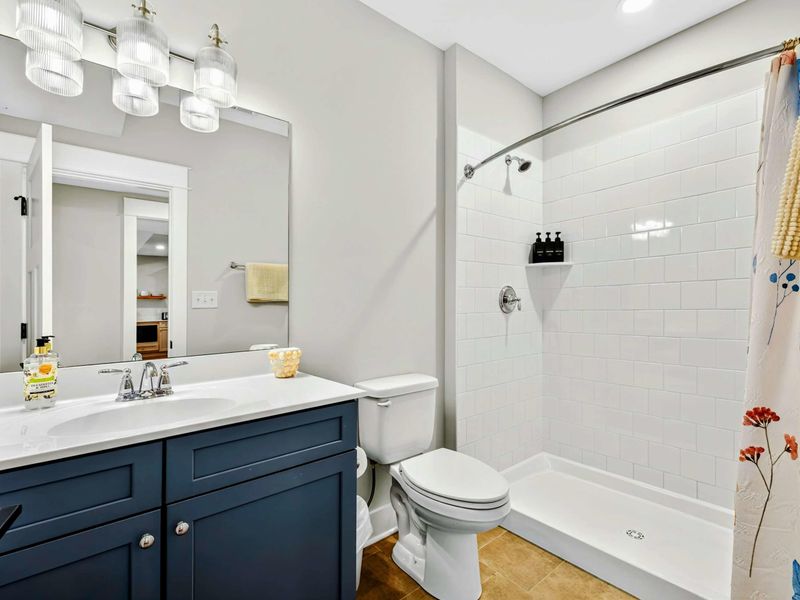 Lower Level Ensuite - A navy vanity with quartz countertop, white subway tile shower, floral curtain, and clean finishes in this lower-level bath.