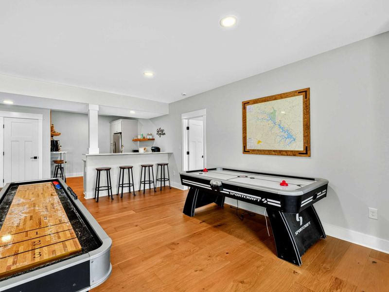 Game Area Overview - Shuffleboard, air hockey, a framed Lake Anna map, and the second kitchen bar with stools create a full entertainment zone on the lower level.