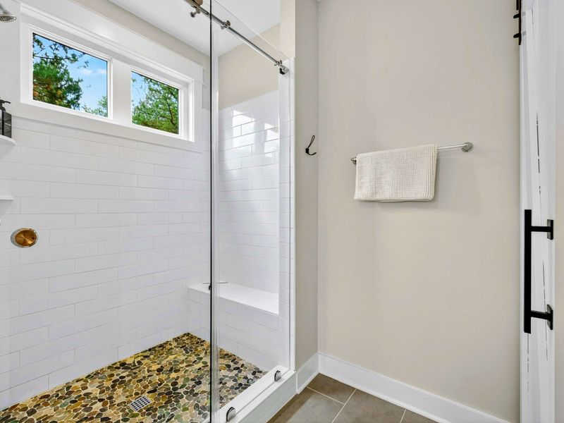 Primary Ensuite Shower - A glass-enclosed walk-in shower with white subway tile, pebble stone floor, and a window for natural light.