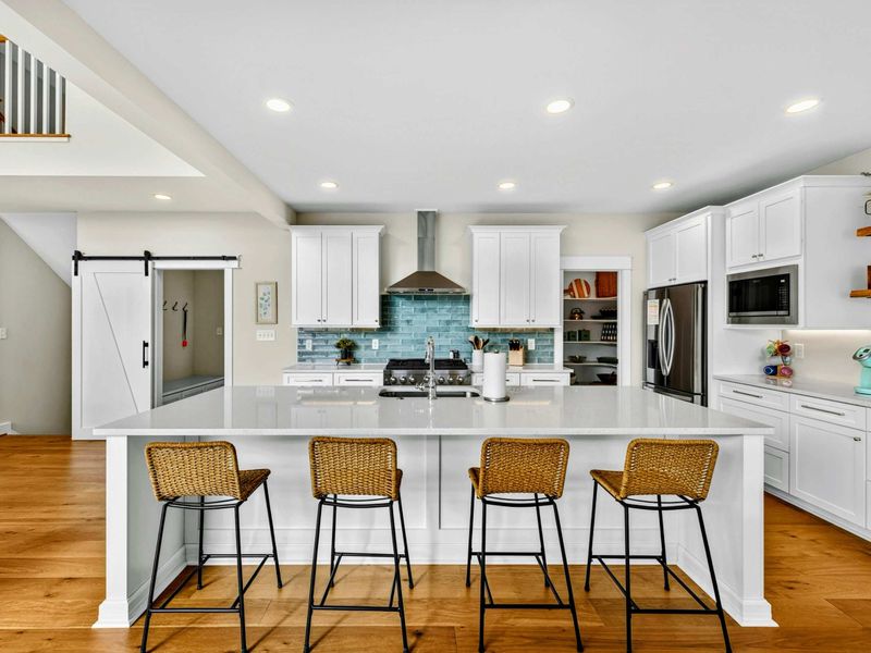 Kitchen A designer kitchen worthy of the view! The oversized island with wicker barstools, crisp white cabinetry, teal tile backsplash, and professional-grade range create an elevated lake-house vibe that's perfect for gathering & entertaining.