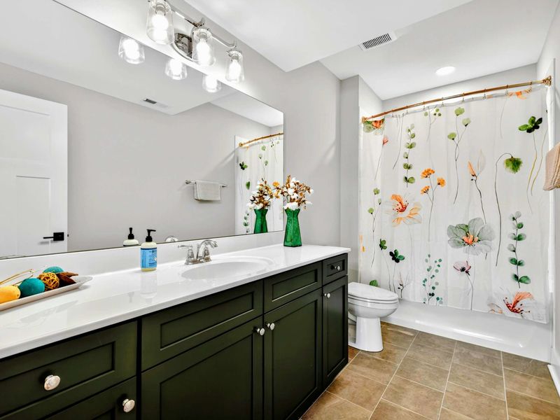 Master Lower Bath - A dark green vanity with quartz countertop, floral shower curtain, and styled accents.