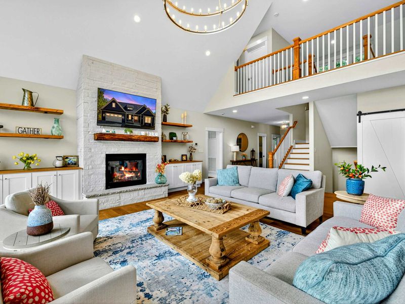 Fireplace Wall - A stone fireplace with a live-edge mantel, floating shelves, built-in cabinets, and a wall-mounted TV create a cozy focal point beneath the loft.
