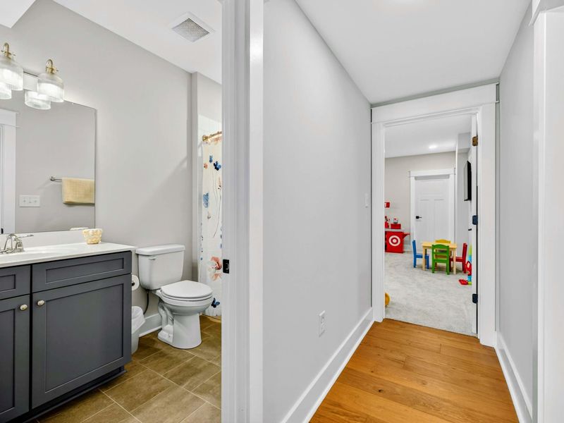 Lower Hallway - The hallway between a lower-level bathroom (dark vanity, playful shower curtain) and the bunk room, with kids'  toys visible ahead.