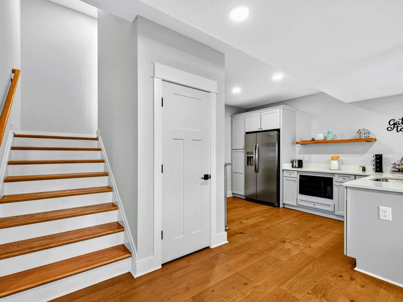 Lower Level Staircase - The staircase to the main level alongside the second kitchen with its full-size refrigerator, microwave, and pantry closet.