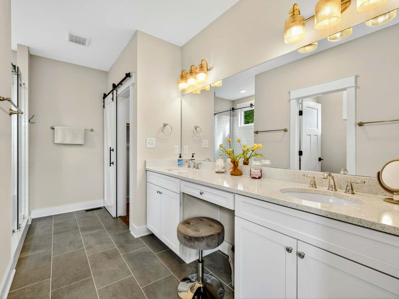 Primary Ensuite Vanity - The double vanity head-on, with twin mirrors, gold sconce lighting, quartz counters, and a seated vanity area between the sinks.