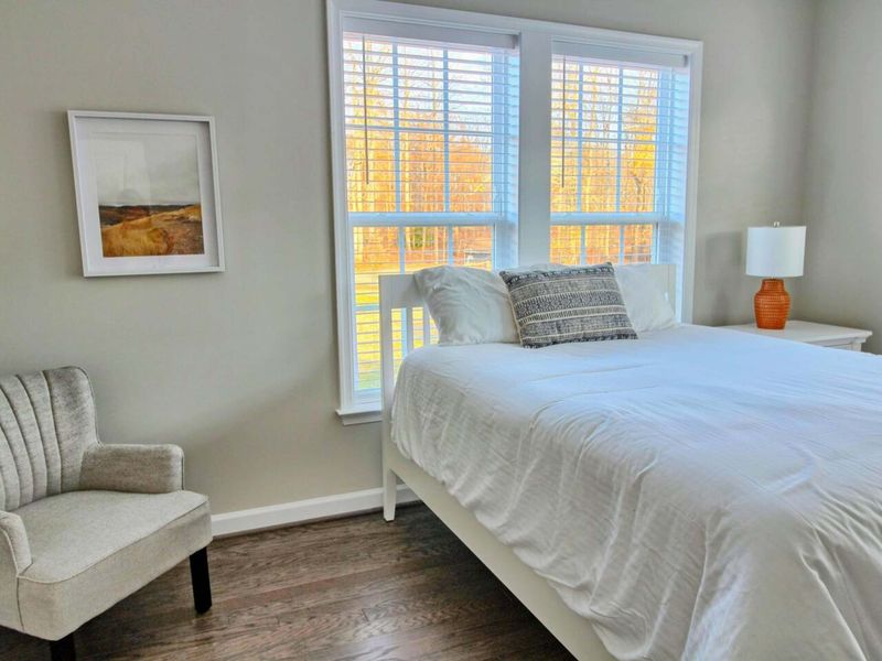 Upper Queen Bedroom - Soft white linens, an upholstered chair by the window, and quiet morning light through wide blinds.