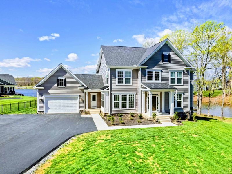 Front Approach - Crisp gables, a covered entry, and lake water visible just past the driveway.