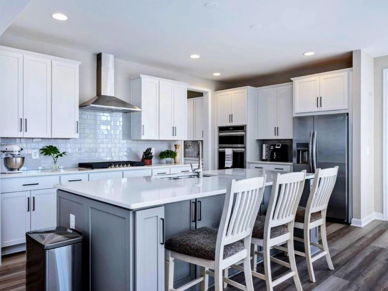 Chef's Kitchen - Wide white island, gas cooktop with stainless hood, and counter seating for casual meals or pre-dinner drinks.