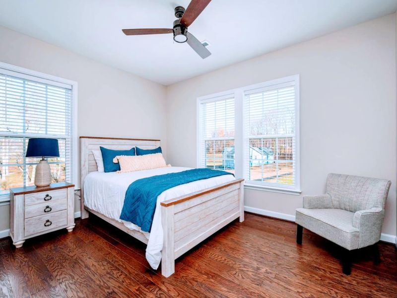 Upper Queen Bedroom - Whitewashed queen with navy throw and pillows, two windows, and a sitting chair tucked in the corner.