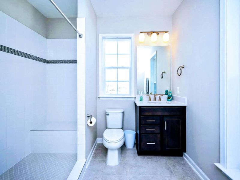 Guest Bath - Tiled walk-in shower, brass fixtures over a dark vanity, and natural light from the window above the toilet.