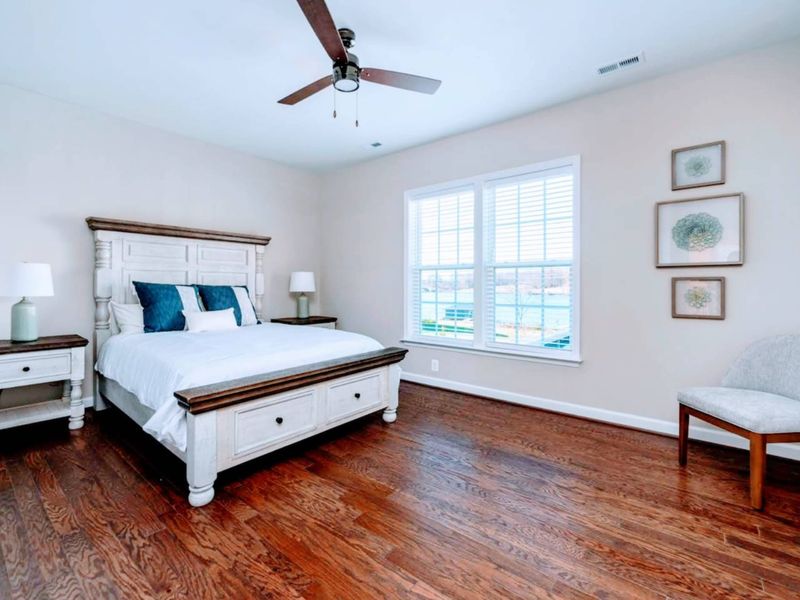Upper Queen Suite - Queen bed with a turned-post frame, lake-view windows, and a sitting chair for quiet morning coffee.
