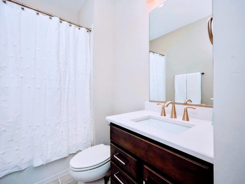 Guest Bath - Tub-shower combo behind a textured curtain, dark vanity with brass fixtures, easy access from the upper bedrooms.