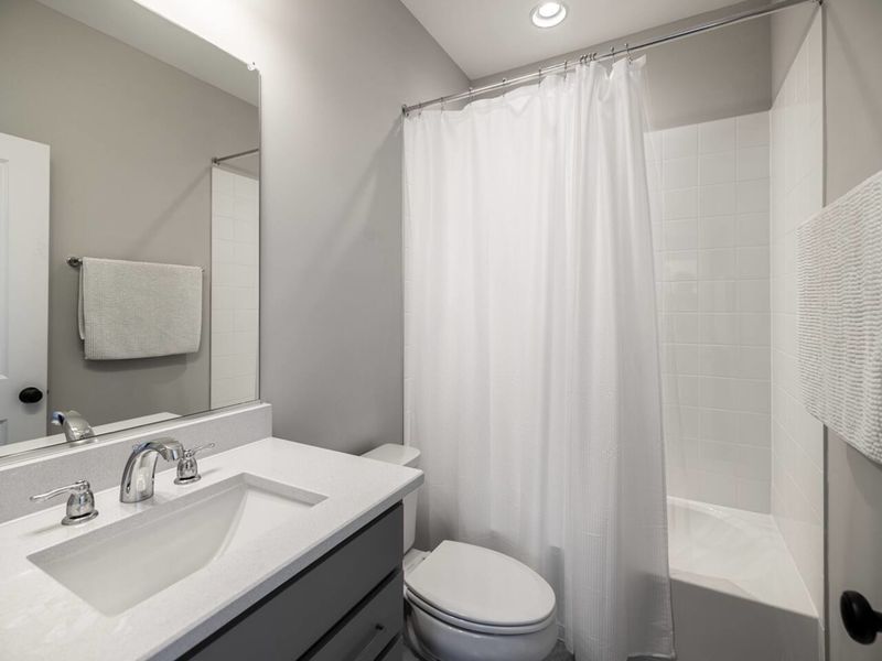 Freshen up in our sleek bathroom featuring a pristine bathtub, modern fixtures, and a well-lit vanity area for a relaxing and comfortable stay