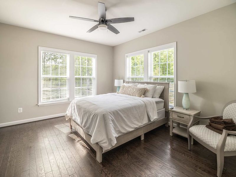 Rest in comfort in this serene bedroom, complete with a plush queen bed, ceiling fan, and abundant natural light for a peaceful retreat