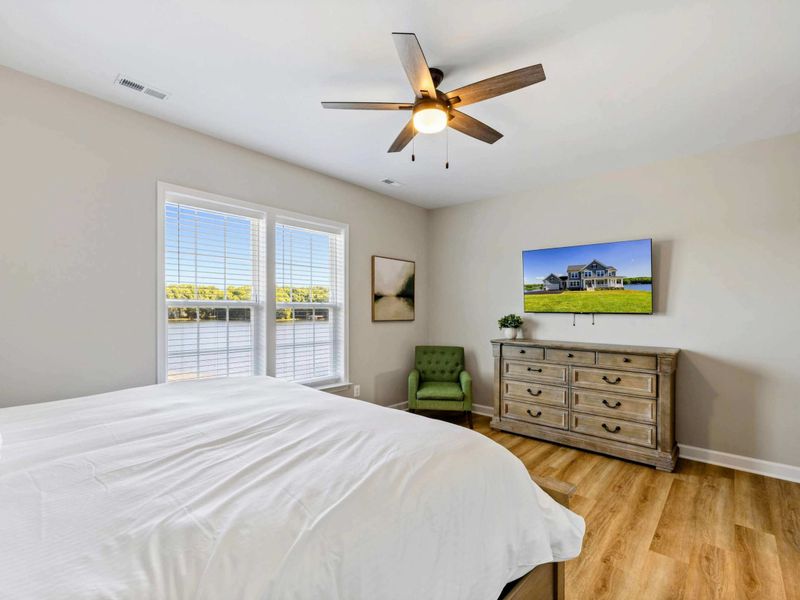 Elegant bedroom with a king-size bed, ceiling fan, wall-mounted TV, and picturesque lake views