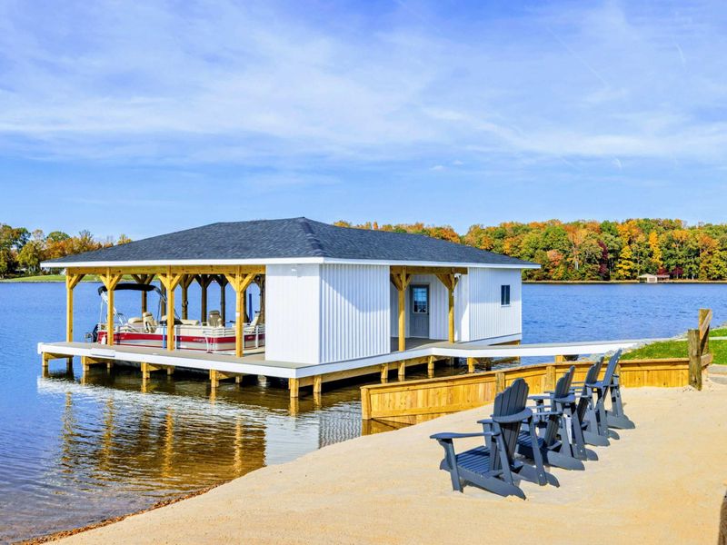 A lakeside boathouse with a sandy seating area featuring Adirondack chairs, perfect for relaxing and taking in the scenic views