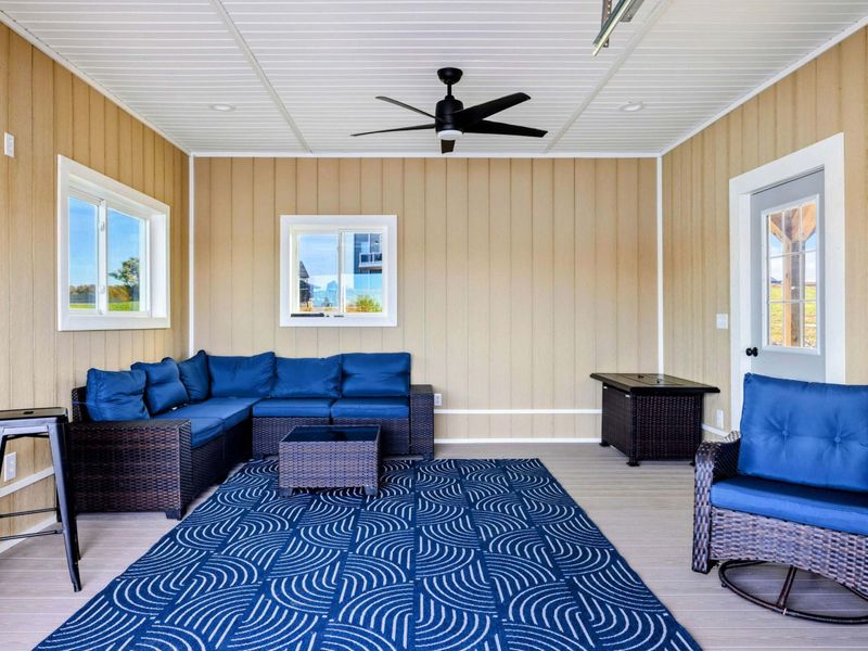 A cozy and stylish lakeside sitting area with plush blue seating, a patterned rug, and a ceiling fan for comfort