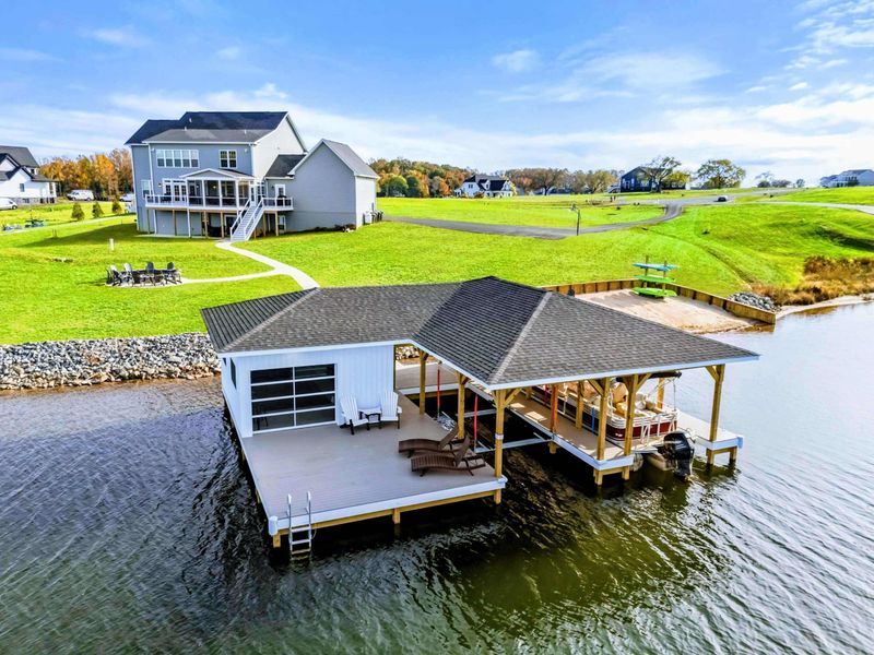 A beautiful lakefront boathouse with a spacious deck, lounge seating, and covered boat slips, perfect for enjoying outdoor activities