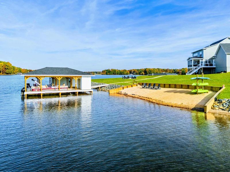 A relaxing lakeside area featuring a sandy beach, paddleboard storage, and a charming boathouse, perfect for water activities and sunbathing