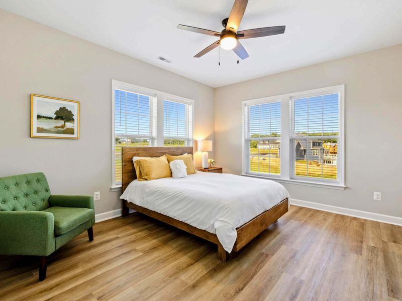Bright bedroom with a queen-size bed, ceiling fan, and large windows providing natural light
