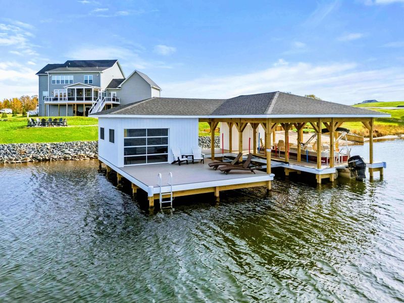 A spacious waterfront boathouse with lounge chairs, a covered seating area, and easy water access, perfect for lakefront relaxation