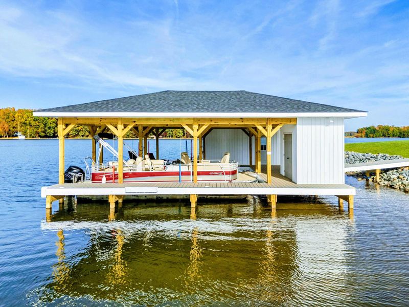 A covered lakeside boathouse with a docked pontoon boat, perfect for water adventures and leisurely lake days