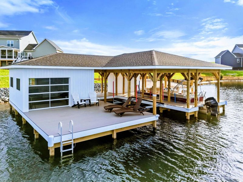 A luxurious lakeside boathouse with a spacious deck, lounge chairs, and a covered boat dock, perfect for enjoying the water