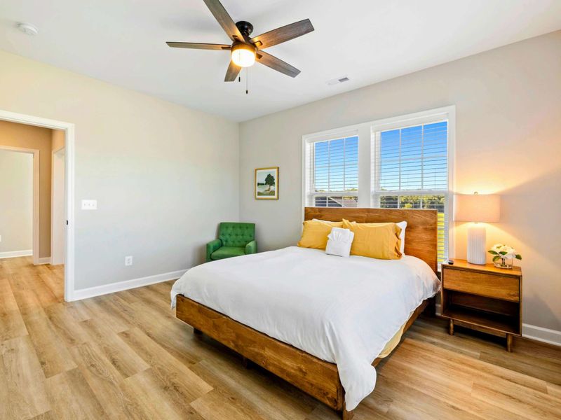 Bright bedroom with a queen-size bed, ceiling fan, and large windows providing natural light