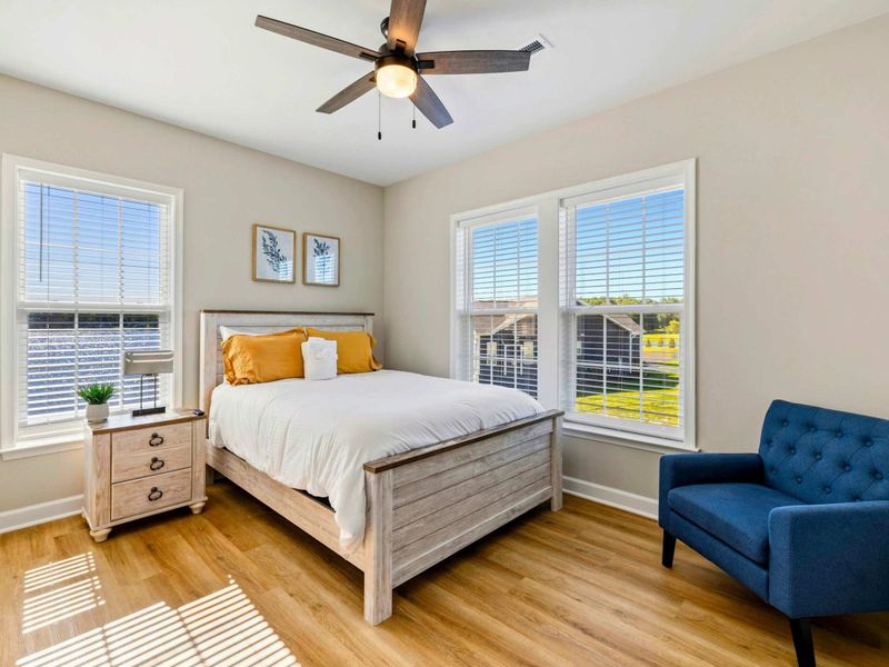 Bright bedroom with a queen-size bed, ceiling fan, and ample natural light from large windows