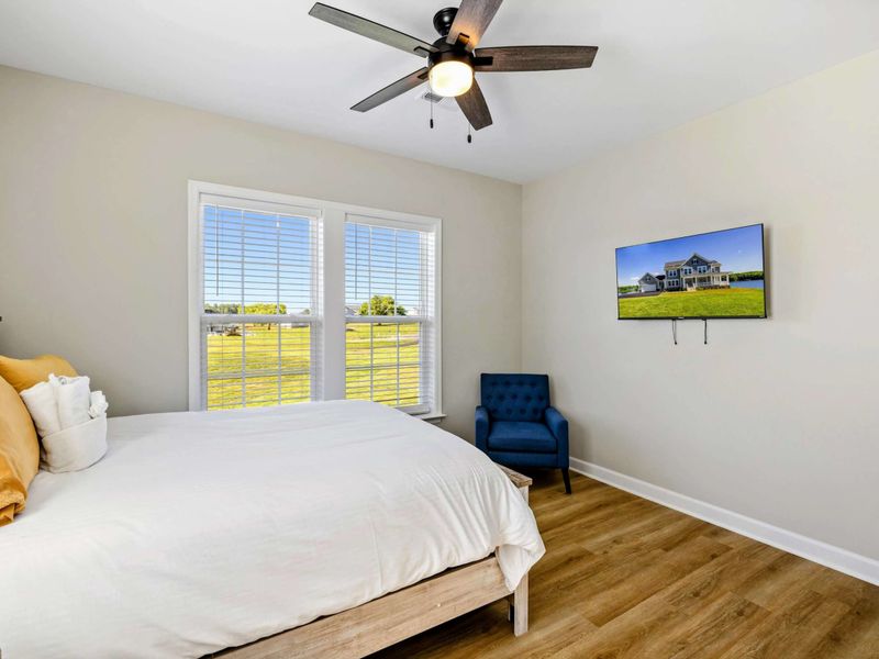 Bright bedroom with a queen-size bed, ceiling fan, and ample natural light from large windows