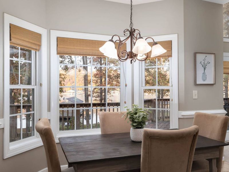 Dining Room - Bay window dining area with a dark wood table, upholstered chairs, woven roman shades, and a wrought iron chandelier.