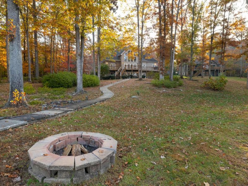 Backyard - Stone fire pit in the fall foliage with a winding path leading back to the elevated deck and home through the trees.