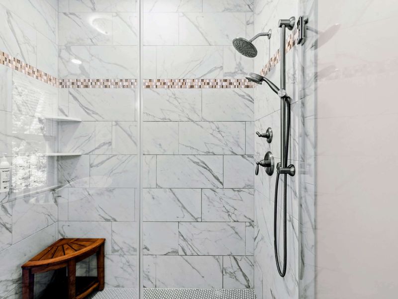 Primary Bathroom - Detailed look at the marble-tile shower with rainfall and handheld fixtures.